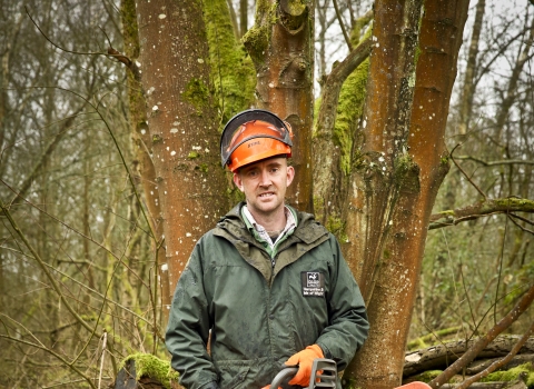 Adam stands with a chainsaw in a wood