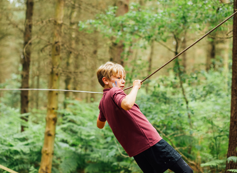 A young boy on an outdoor adventure course in a woodland